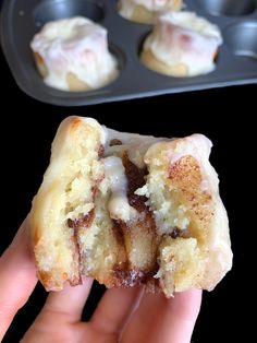 a hand holding a half eaten doughnut in front of a muffin tin filled with cupcakes