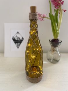 a bottle with lights inside sitting on a table next to a vase filled with flowers