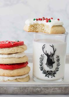 a stack of cookies next to a glass of milk with a reindeer cookie on top