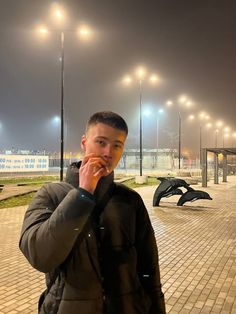 a man is standing in front of some benches at night, talking on his cell phone