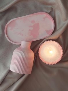 a small pink vase next to a lit candle on a gray cloth covered tablecloth