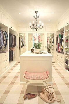 a walk in closet with lots of clothes and handbags on the floor, chandelier hanging from the ceiling