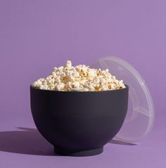 a black bowl filled with popcorn on top of a purple background