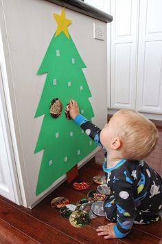 a toddler playing with a christmas tree made out of paper and magnets on the fridge