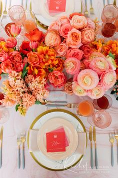 the table is set with pink and orange flowers, gold place settings, and silverware