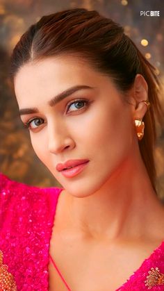 a woman with blue eyes and pink dress posing for a photo in front of a gold background