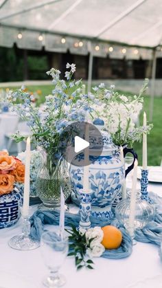 a table topped with blue and white vases filled with flowers next to tall candles