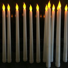 many white candles are lined up in a row with one candle glowing yellow and the other lit orange