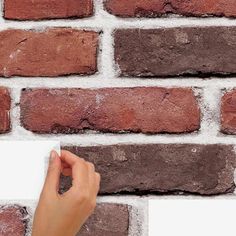 a hand is holding a piece of paper in front of a brick wall that has been made from red bricks