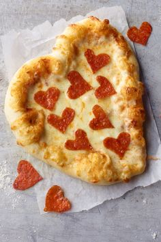 a heart shaped pizza sitting on top of a piece of wax paper with hearts drawn on it