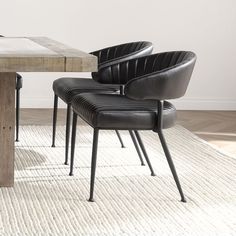 two black chairs sitting at a wooden table in front of a white rug and wall