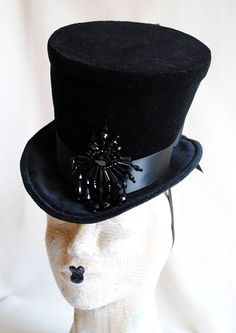 The Tease is a fabulous dark fashion lady's top hat,luxuriously elegant and feminine all the way! It is covered with rich black velvet and trimmed with black ribbon around the crown that ends in a beautiful double black bow at the back. The focal point is a majestic hand-beaded black crystal element at the side front that sparkles as you move around. Measurements : height 6.5 inches( 16 cm ) front to back 9 inches ( 23 cm ) side to side 8 inches ( 20 cm ) THIS IS NOT A FIT TO HEAD HAT NOT SUITAB Fitted High Crown Costume Hats And Headpieces, Fitted Fantasy Hat For Costume Party, Fitted Top Hat For Halloween Costume, Vintage High Crown Top Hat For Costume Party, Gothic Costume Hat With Round Crown For Costume Party, Vintage Top Hat For Costume Party, Fitted High Crown Costume Hat For Carnival, Fitted High Crown Hat For Carnival, Gothic Fitted Costume Hats And Headpieces