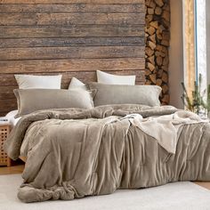 a bed covered in blankets and pillows next to a wooden wall with logs on it