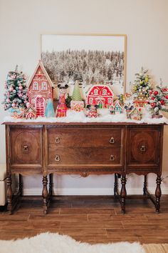 a christmas scene is displayed on the wall above an old dresser with ornaments and trees