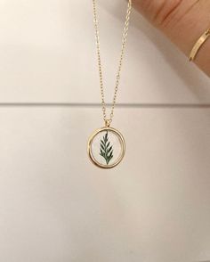 a hand holding a gold necklace with a small green plant in the center on it