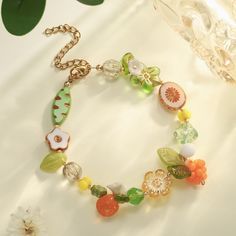 a close up of a bracelet on a table with flowers and fruit charms around it