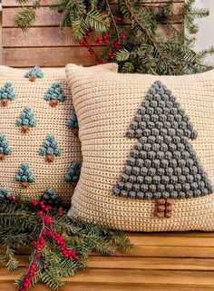 two crocheted christmas pillows on a bench with evergreen branches and pine cones in the background