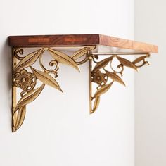 a wooden shelf with metal flowers and leaves on it's sides, against a white wall