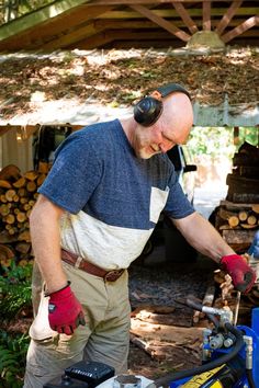 a man with headphones and gloves working on a piece of equipment in front of a pile of logs