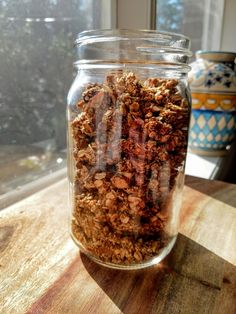 a glass jar filled with granola sitting on top of a wooden table next to a window