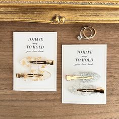 two pieces of paper with gold foil on them next to a pair of wedding rings