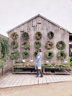 a woman standing in front of a wooden structure with plants growing on the sides and around it