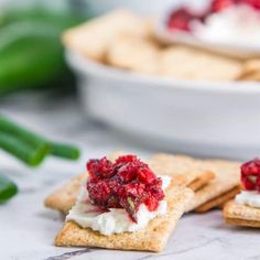 crackers with cranberry sauce and whipped cream on them next to a bowl of cucumbers