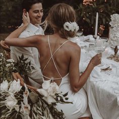 a man and woman sitting at a table with flowers in their hair, one holding the other's hand