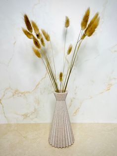 a vase filled with dry grass on top of a counter next to a marble wall