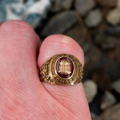 This attractive Kearny High School 1949 class ring is centered with an oval cabochon cut lab created ruby gemstone. The ruby is then centered with a gold appliqué. The shoulders of the ring are decorated with rams and great etchings. The ring is crafted of 10k yellow gold with a nice unpolished patina. Gold Ruby Ring Oval Cabochon With Polished Finish, Yellow Gold Ruby Signet Ring With Polished Finish, Gold Ruby Signet Ring With Polished Finish, Vintage Red Signet Ring With Oval Cabochon, Vintage Red Oval Cabochon Signet Ring, Antique Yellow Gold Ruby Ring With Polished Finish, Vintage 14k Gold Ruby Ring With Polished Finish, Heirloom Ruby Signet Ring With Hallmark, Vintage Ruby Rings With Polished Finish