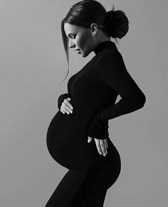 the pregnant woman is posing in her black dress and tight pants with her hands on her hips