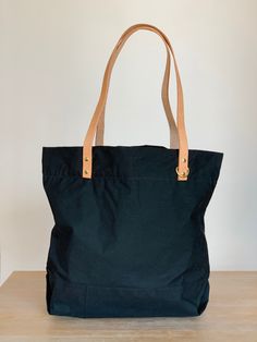 "The Portsmith tote is a great casual canvas tote bag for everyday use. It is perfect for all your shopping, traveling, and work needs! It is large, so it can comfortably fit your laptop, lunch, and water bottle. This black Portsmith tote bag was made with waxed canvas with tan leather straps. This tote bag can stand on its own, so it's great when you need to pile everything you need into it. Waxed canvas shows its wear and use, so expect to see folds, cracks, scratches, wrinkles, and creases. The bonus to waxed canvas is that it is also water-resistant. These are waxed canvas's natural characteristics!  The interior features a 100% cotton lining and a medium-sized black waxed canvas pocket. The D-ring on the front is great to attach your keys to.  Each bag is made with materials bought fr Black Cotton Weekender Bag For Everyday Use, Casual Everyday Canvas Bag With Waxed Finish, Eco-friendly Waxed Canvas Tote Bag, Waxed Canvas Tote Bag For Everyday Use, Waxed Finish Canvas Tote Bag For Everyday Use, Everyday Waxed Finish Canvas Tote Bag, Waxed Canvas Bag With Canvas Lining For On-the-go, Eco-friendly Canvas Bag With Leather Handles For Everyday Use, Large Capacity Waxed Canvas Weekender Bag