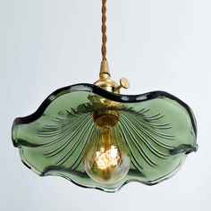 a green glass light fixture hanging from a corded ceiling with a white wall in the background