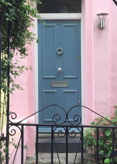 a blue door is in front of a pink house with wrought iron fence and gate