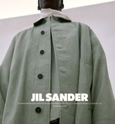 a man is wearing a green coat and standing in front of a white wall with the words jil sander on it