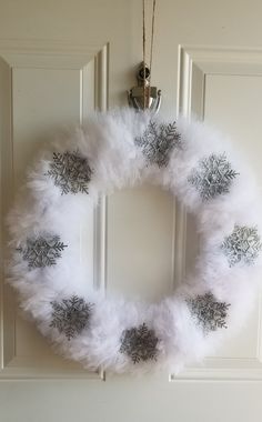 a white wreath with silver snowflakes hanging from it's side on a door