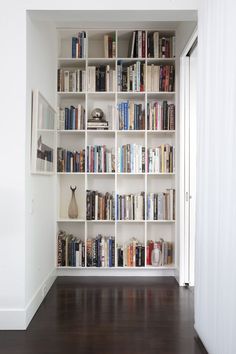 a book shelf filled with lots of books on top of a hard wood floor next to a white wall