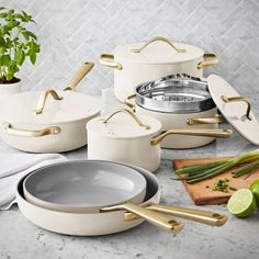 white pots and pans with gold handles on a marble countertop next to a cutting board