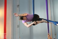 a woman is performing aerial acrobatic tricks on the rings in an indoor gym