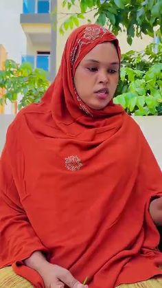 a woman sitting on the ground wearing a red head scarf