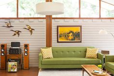 a living room with green couches and two birds on the wall above them,