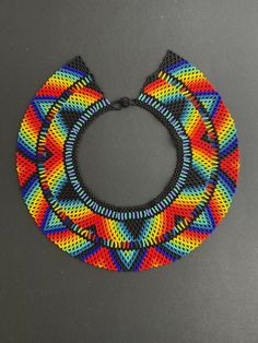 This Elegant and Colorful Choker was made by the Embera Chami tribe of Colombia using ancestral beading techniques. Their pieces are all handmade, and the designs and colors used are unique to their tribe and related to their everyday lives.   This is a one-of-a-kind handmade necklace that would surely have people admiring it any time you wear it, making it the perfect eye-catching piece your wardrobe needs.  Color: Blues, Black, Yellow, Red, and Orange Length:16" Width: 3" Check out other simil Traditional Multicolor Beaded Necklaces As Gift, Traditional Colorful Beads For Crafting, Multicolor Fair Trade Beads For Festival, Traditional Handmade Bib Necklace With Round Beads, Traditional Handmade Multicolor Beads, Multicolor Festival Beads, Traditional Handmade Multicolor Beaded Necklaces, Traditional Beaded Chain For Crafting, Bohemian Rainbow Beads For Jewelry Making