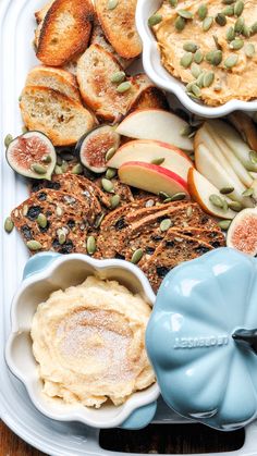 an assortment of food is displayed in bowls on a tray with bread, apples, and pumpkins