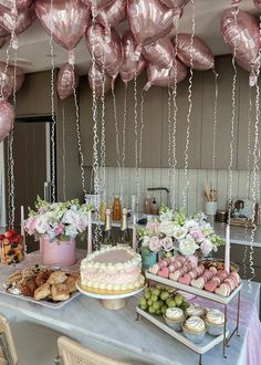 a table topped with lots of cakes and desserts next to balloons hanging from the ceiling