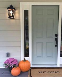 two pumpkins are sitting on the front porch next to a welcome mat and lantern