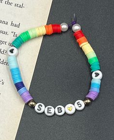 a colorful bracelet with beads that spell out sebs on it's side and an open book in the background