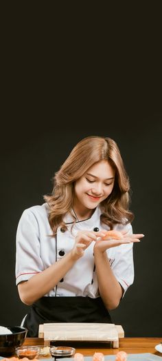 a woman in chef's uniform is looking at her cell phone while standing next to some sushi