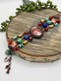 a necklace is sitting on top of a piece of wood with beads and charms hanging from it