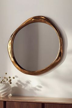 a round mirror sitting on top of a wooden table next to a vase and flower