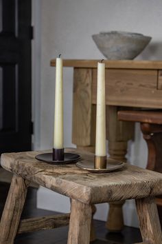 two candles sitting on top of a wooden table in front of a bowl and chair